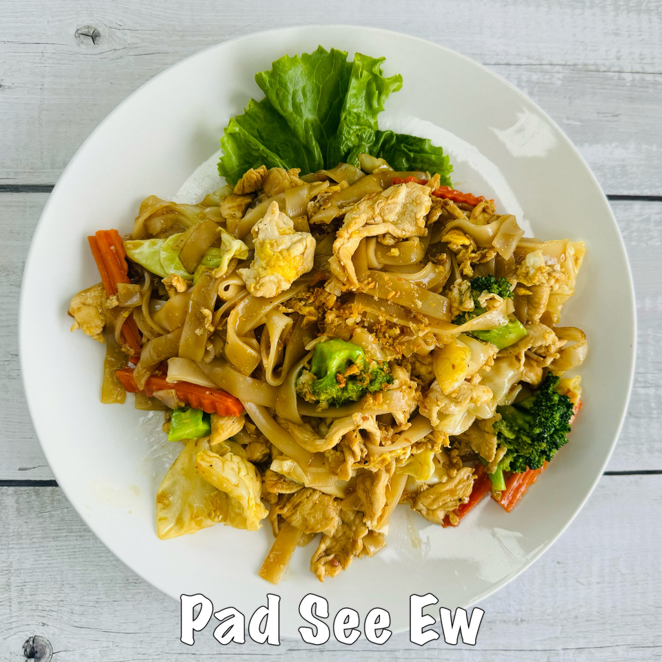 A white plate of Pad See Ew with wide noodles, chicken, broccoli, carrots, and cabbage.