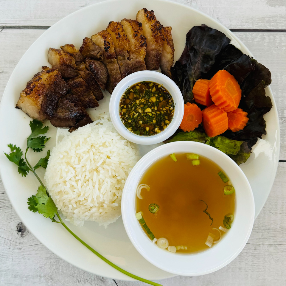 Grilled pork with rice, dipping sauce, soup, carrots, and lettuce on a white plate.