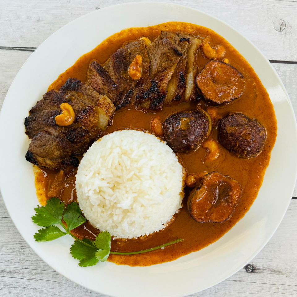 Thai Massaman Curry with grilled beef, potatoes, cashews, and white rice, garnished with cilantro.