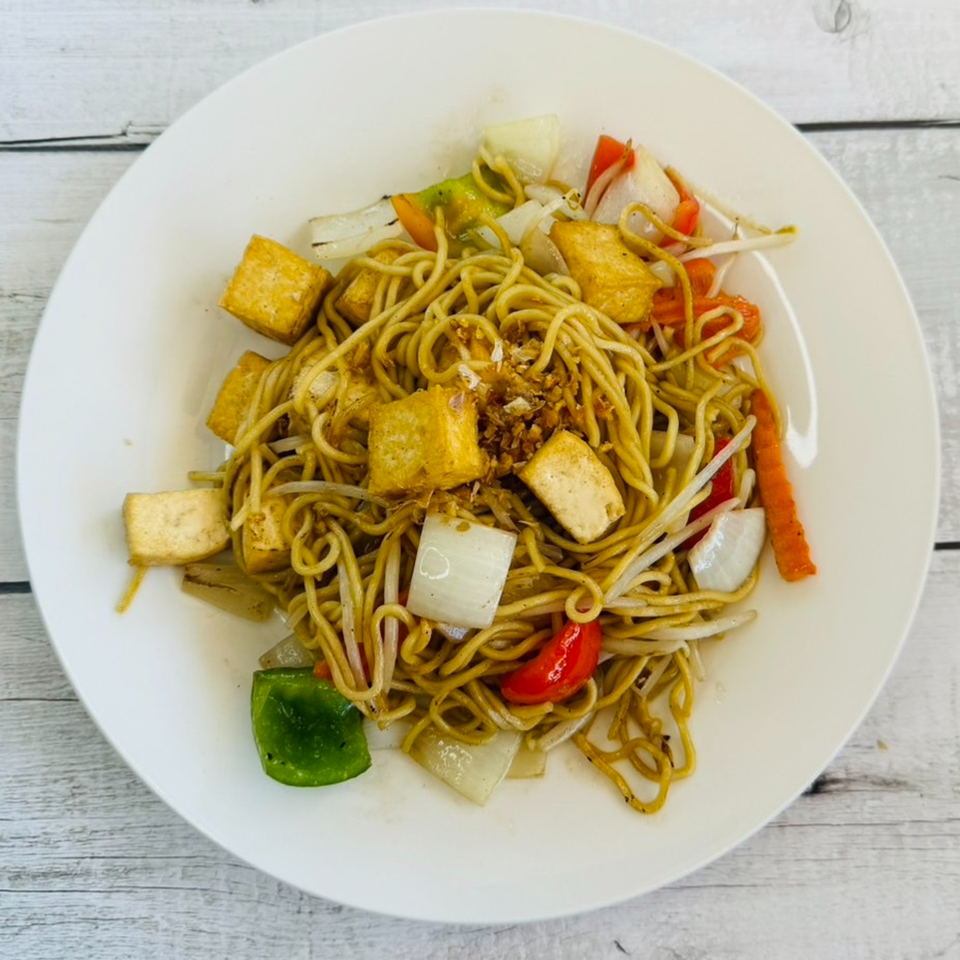 A white plate of Thai stir-fried noodles with tofu, onions, bell peppers, and bean sprouts.