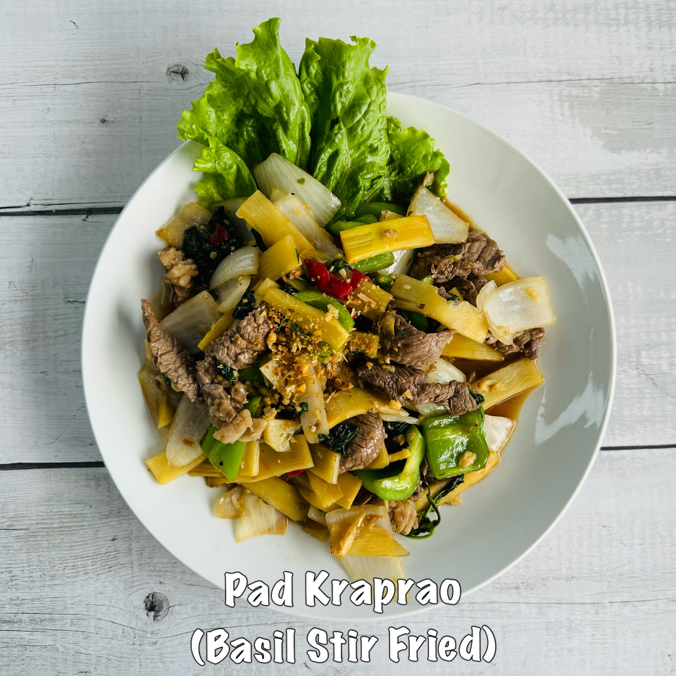 A white plate of Pad Kraprao, a Thai basil stir-fry with beef, bamboo shoots, and vegetables.
